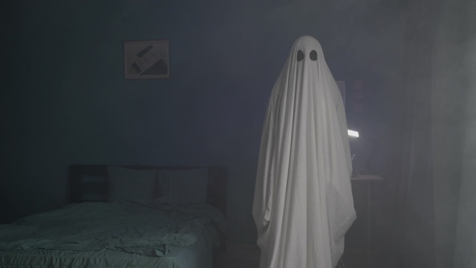 雾中黑暗房间里可怕的幽灵。披着被单的恶魔。万圣节的概念。