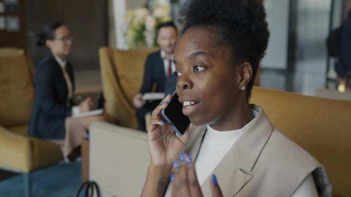 美丽的非洲裔美国女士在现代酒店大堂的室内用手机谈论旅行
