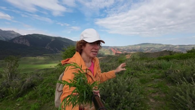 女视频博主手持采摘的新鲜龙蒿在山上散步的自拍视频