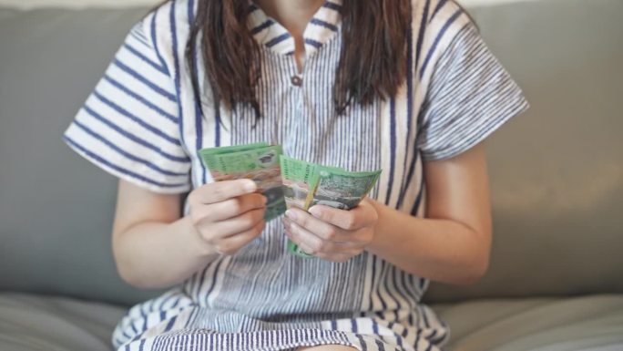 年轻女子坐在沙发上数着澳元钞票、现金。