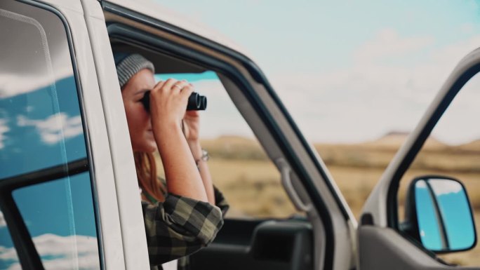 一位美国游客坐在她的露营车里，用双筒望远镜看沙漠