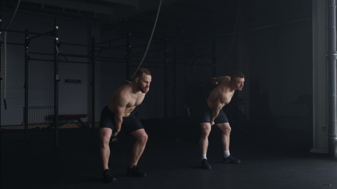 两个肌肉男在健身房举壶铃，专业举重运动员一起训练