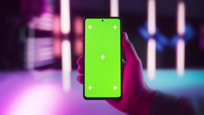 视频游戏玩家手持绿色屏幕模拟显示的智能手机的视角。在时尚的霓虹灯房间里，一个人拿着一个设备的第一人称