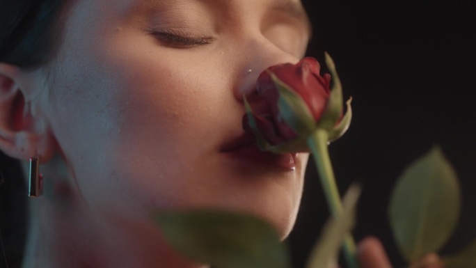 美丽的性感女人与红色的口红黑色背景工作室拍摄的姿势，闻着一朵红玫瑰和调情的镜头