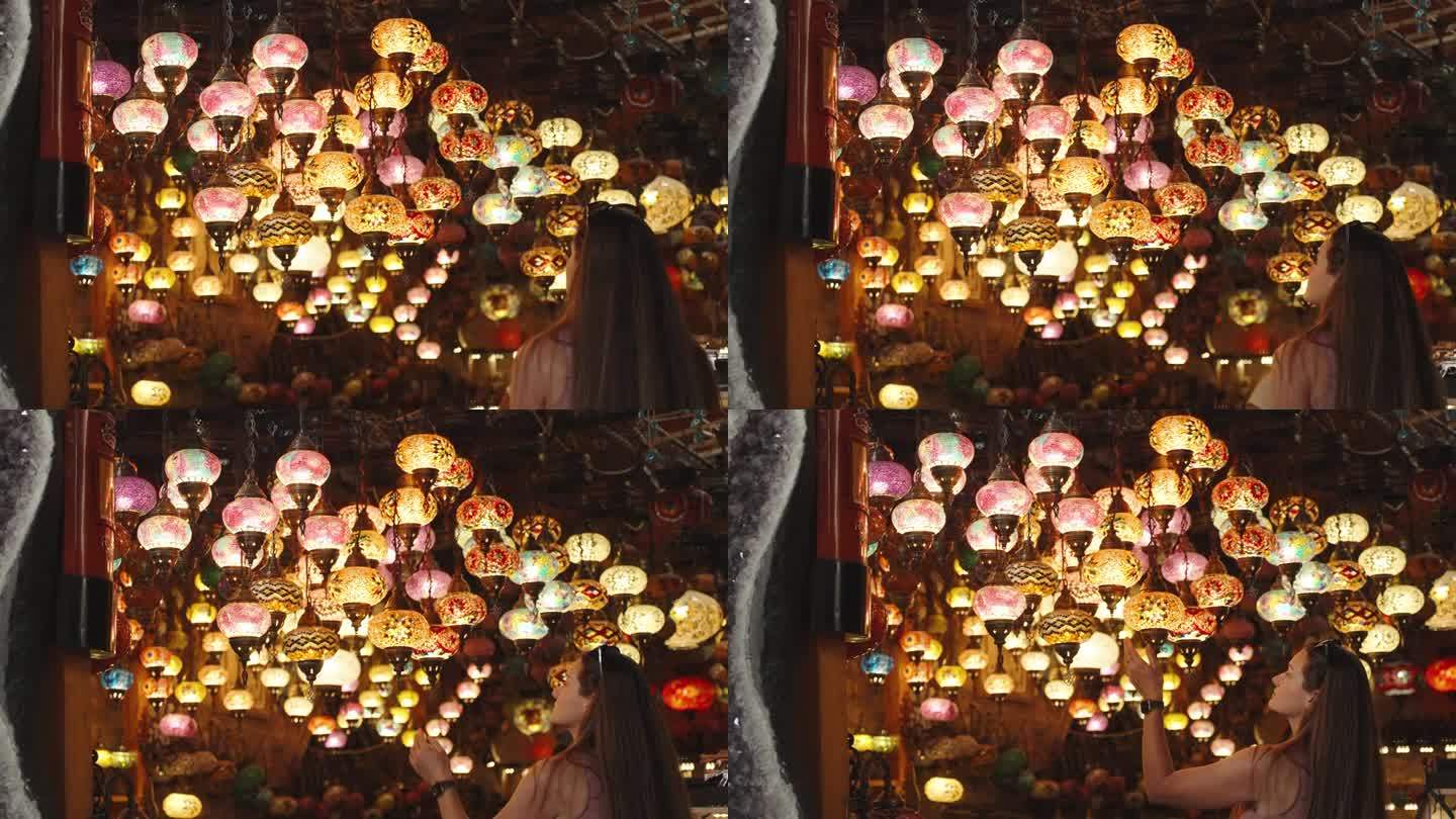 一名年轻女子走进一家土耳其纪念品商店，天花板上挂着彩色玻璃制成的吊灯。