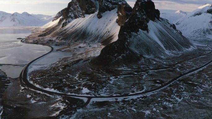 无人机拍摄倾斜在沿海道路和高耸的山峰，阳光明媚，冰岛的冬夜