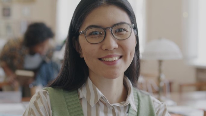 聪明的亚洲女学生的肖像，在高中图书馆看着相机微笑