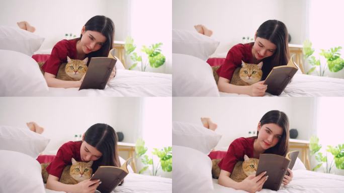 亚洲妇女抱着小猫在家里快乐地玩耍。迷人美丽的女人躺在床上，在卧室里和她温柔的宠物一起度过闲暇时光读书