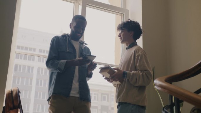 慢动作的年轻男子学生在大厅见面打招呼，用平板电脑交谈