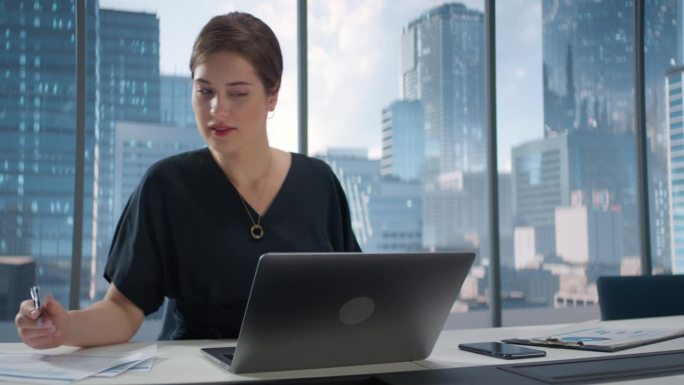年轻成功的白人女商人的肖像，坐在办公桌旁用笔记本电脑工作。女经理策划电子商务项目投资策略。