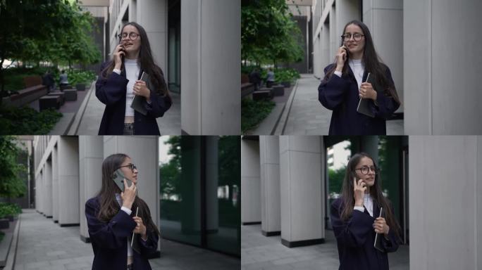 一位留着长发的年轻女子，穿着经典的休闲装，戴着眼镜，走在市中心的办公楼附近，拿着平板电脑，微笑着讲着