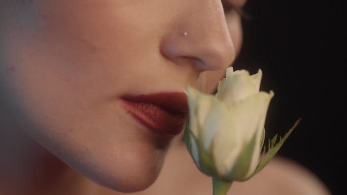 美丽的感性的女人与红色的口红黑色背景工作室拍摄的姿势与一个单一的白玫瑰。闻花香