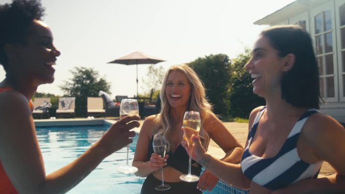 一群成熟的女性朋友穿着泳装在泳池里喝着香槟酒