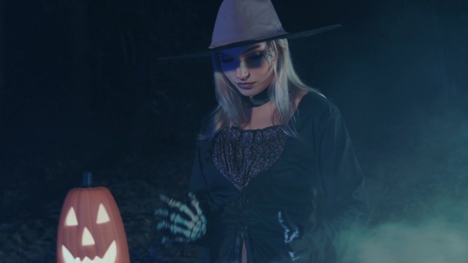 戴着帽子和斗篷的神秘女巫师在她的坩埚里施咒，为万圣节做准备