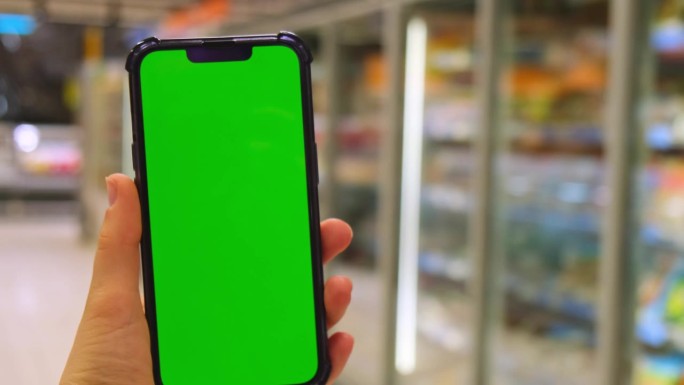 4k手机色度键用于手机应用程序。商场商店里，女士手持绿屏智能手机的特写。在超市、网上杂货店购买冷冻食