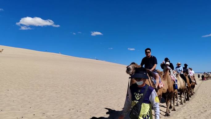 在沙漠旅游区骑骆驼的游客排成排