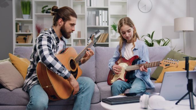 音乐老师和十几岁的学生女孩坐在沙发上学习吉他演奏新歌在私人课程在明亮的客厅或音乐工作室。