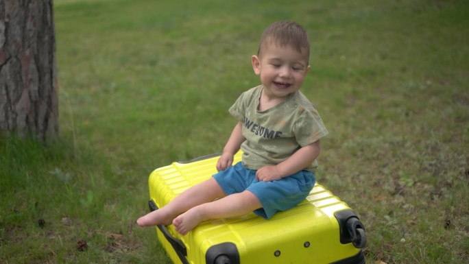 一个小男孩坐在一个黄色的手提箱里。一个一岁大的孩子坐在行李箱上滚了下来。4 k