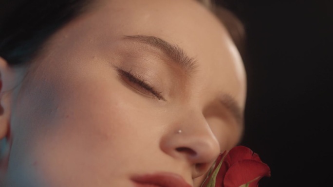 美丽性感的女人用红色的口红黑色的背景工作室拍摄的姿势亲吻一朵红玫瑰和调情的镜头