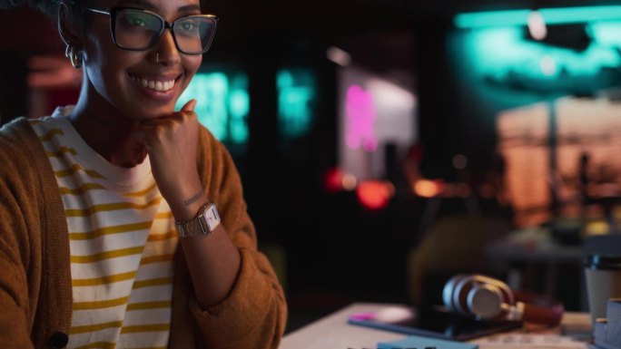 年轻的黑人女商人在创意机构的特写肖像，微笑和电脑在办公室在晚上。才华横溢的女性开发者与初创公司合作开