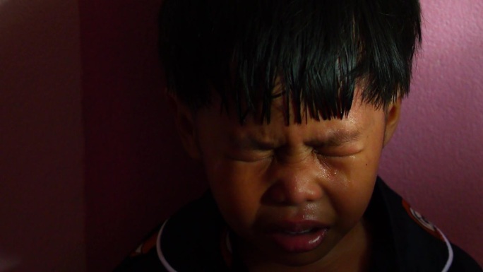 一个小男孩坐在家里角落的阴影里，悲伤地哭泣。