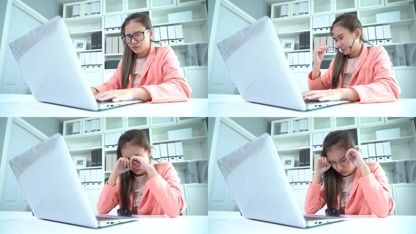 严肃的亚洲年轻女商人在办公桌上使用笔记本电脑，眼睛疲劳疼痛，摘下眼镜，揉着眼睛。疲惫不堪的工人闭上眼
