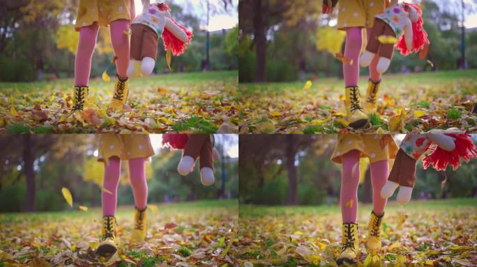 秋天的公园里，顽皮的女孩带着布偶布娃娃在地上散步，玩着五颜六色的秋叶