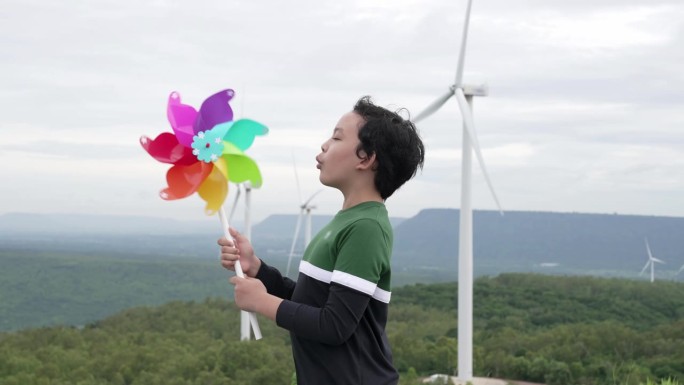进步的年轻亚洲男孩在风力涡轮机农场玩风力涡轮机玩具。