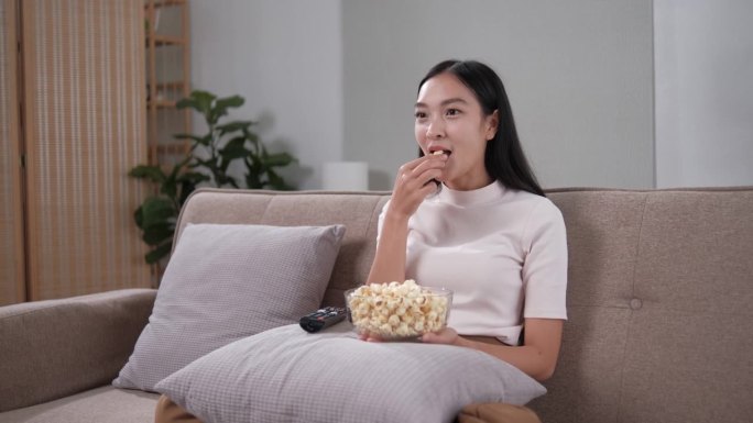 亚洲年轻漂亮的女人在家里看有趣的电视电影。有吸引力的休闲女孩感到快乐和放松。