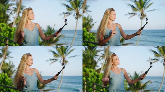 金发美女旅游博主在热带岛屿上用自拍相机拍摄自己的侧视图，可以看到海洋。斯里兰卡一名女视频博主手持手机