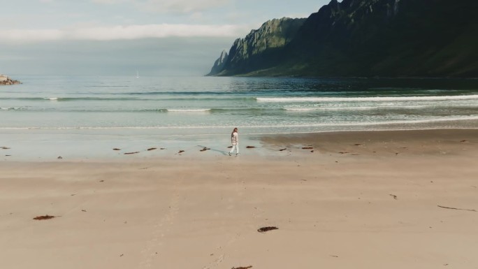 在明媚的阳光下，无忧无虑的少女沿着厄斯峡湾海滩的海岸散步的全景