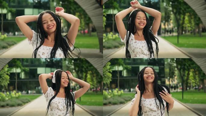一位年轻迷人的非洲女子在公园里戴着耳机跳舞，绕着她的轴线旋转，举起双手。自由，无忧无虑的青春