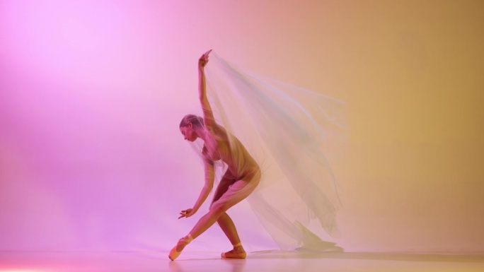 性感和女性气质。美丽的年轻女芭蕾舞演员在霓虹灯下表演透明面纱，反对渐变粉黄色工作室背景