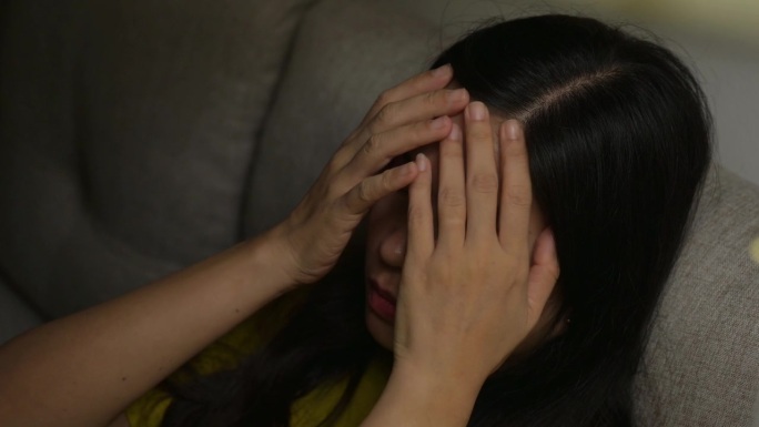 一个亚洲女人痛苦地坐在家里的沙发上哭泣