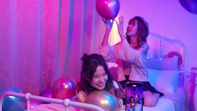 两名亚洲女子在卧室用手机直播视频封面舞蹈。