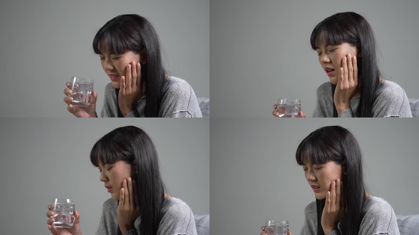 年轻的亚洲女子在喝装有冰块的水时牙痛。医疗保健理念。