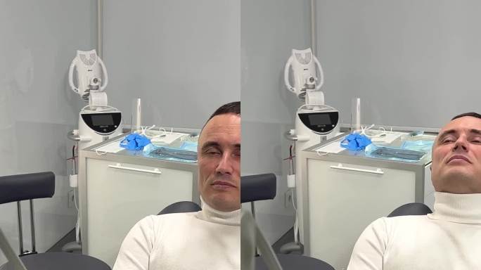 一名男子坐在牙科诊所的牙科座椅上，这名男子双手交叉在胸前，头靠在头枕上，抬头等待专业医生的到来