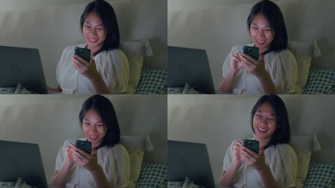 年轻的亚洲女孩晚上坐在家里的床上使用笔记本电脑和手机。失眠、晕机、无手机恐惧症、睡眠障碍。