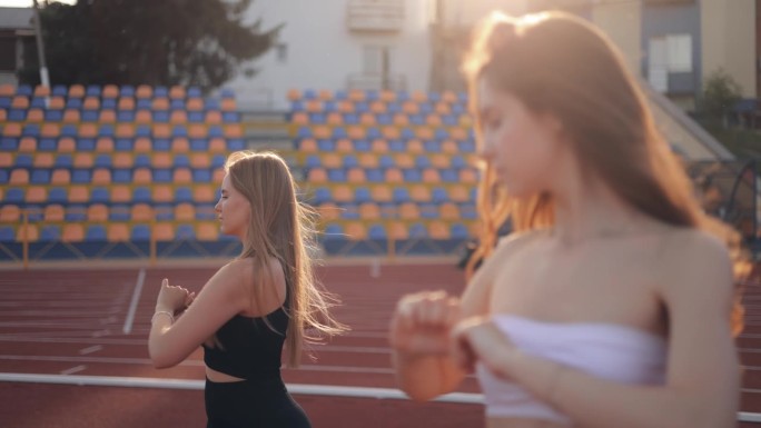 两个运动女孩苗条的朋友来到体育馆慢跑或健身，做热身，互相扶持，在日落时分做手臂练习