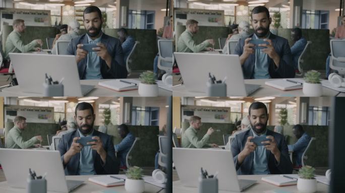 快乐的阿拉伯商人在办公室的办公桌上用智能手机玩在线视频游戏的画像