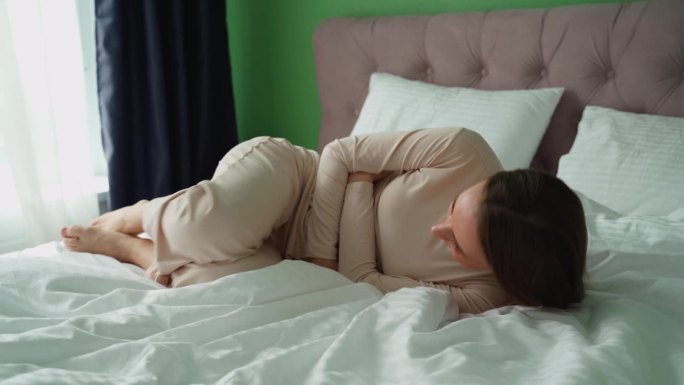 女性疼痛或月经综合症。一名年轻女子躺在家里的床上，捂着肚子克服痉挛。