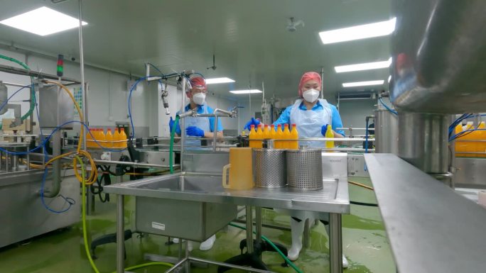 亚洲华人男果汁厂工人在生产线上封橙汁瓶盖