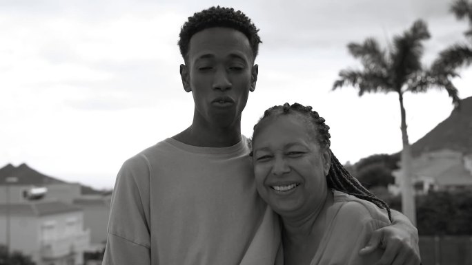 幸福的非洲母亲和成年儿子在家里的阳台上微笑着拥抱在一起——黑白剪辑