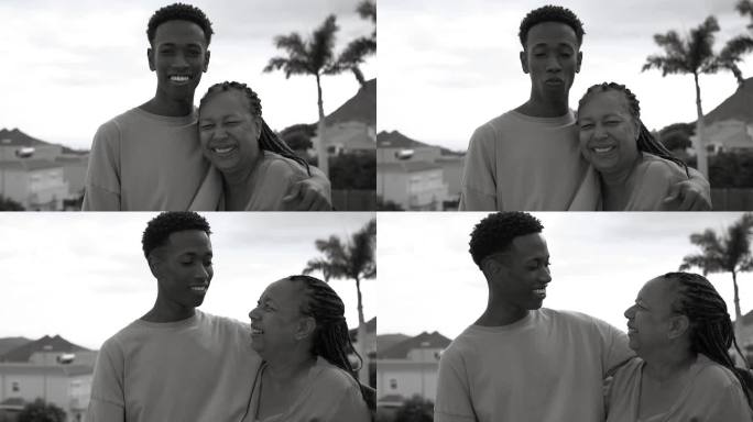 幸福的非洲母亲和成年儿子在家里的阳台上微笑着拥抱在一起——黑白剪辑