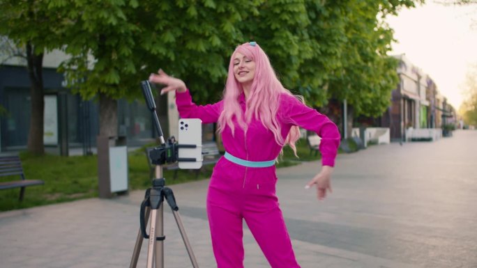 一个穿着粉色衣服的快乐女孩在手机前跳舞，她把手机放在她前面的三脚架上。街上快乐的快闪族