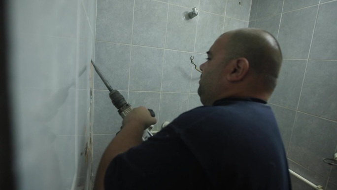 男杂工，用冲击钻拆除客户浴室的瓷砖