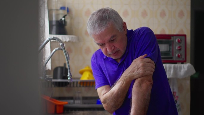 焦虑的老人倚在厨房的水槽上，患有精神疾病。白发老人独自在家与疾病作斗争