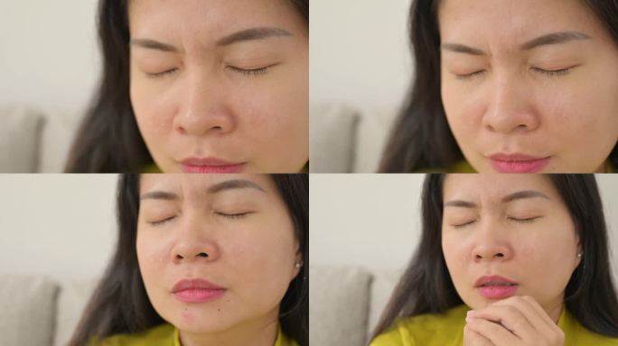 一个亚洲女人痛苦地坐在家里的沙发上哭泣