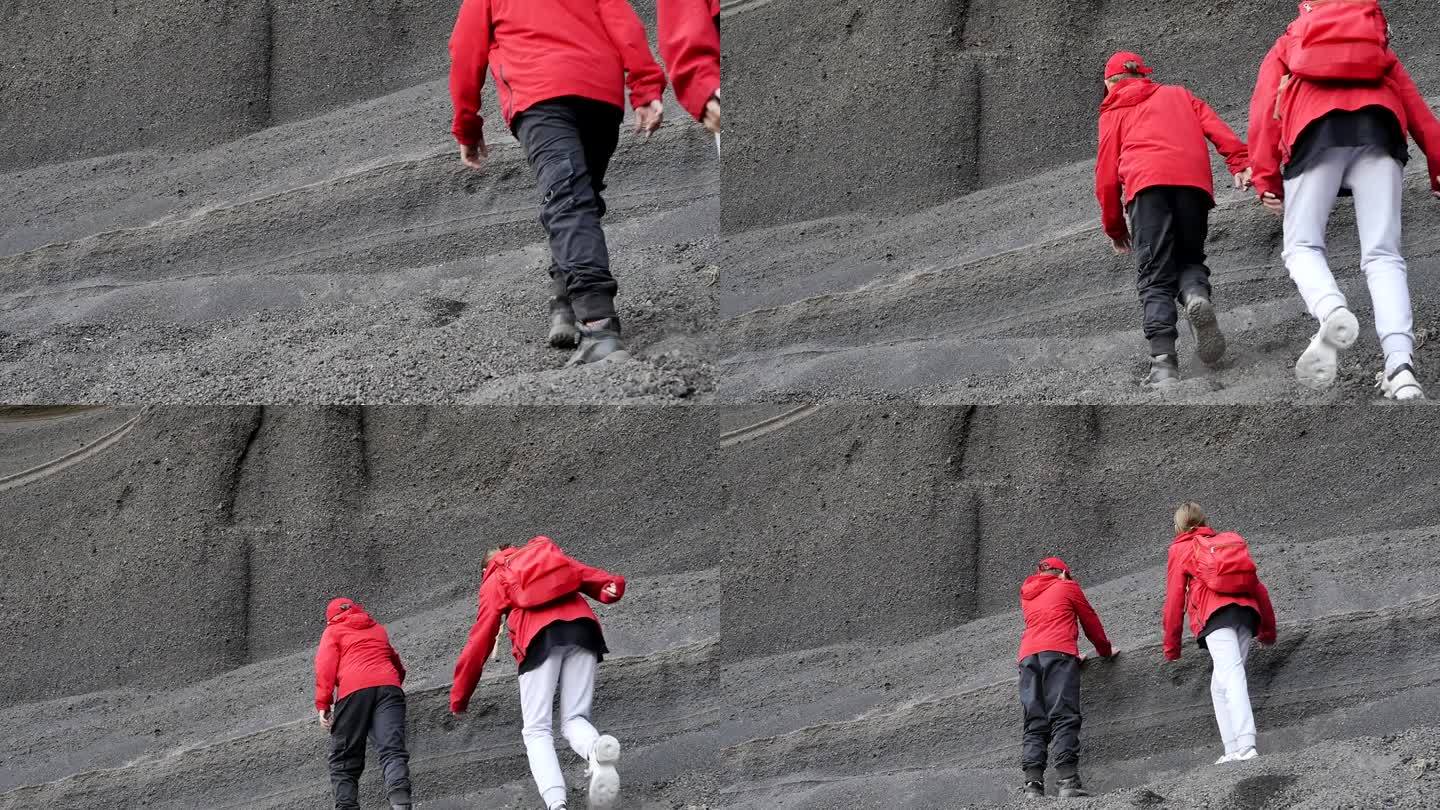 一个小男孩和一个小女孩穿着红色夹克，背着背包，爬上一块由火山灰和古老的死火山渣组成的灰色松散岩石。青