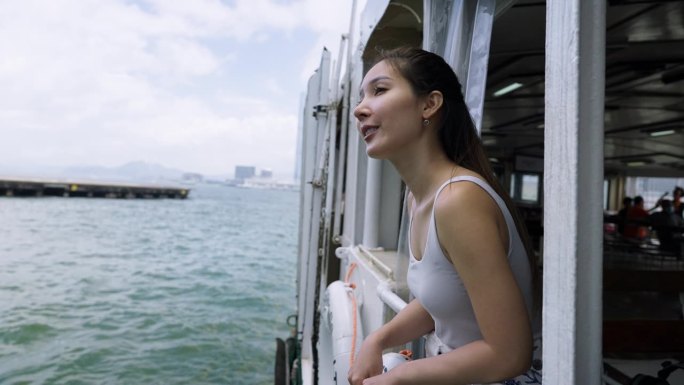 一名年轻的亚洲女子在维多利亚港乘渡轮往窗外看